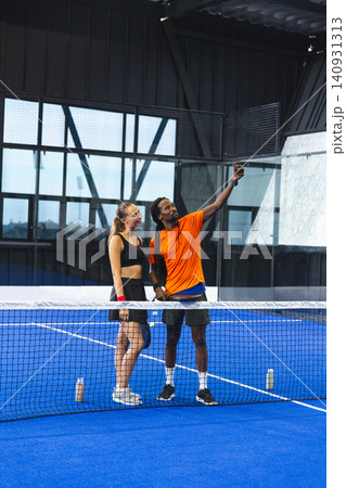 Diverse athletic friends taking selfie on padel court at net with smartphone and water bottles Diverse athletic friends taking selfie on padel court at net with smartphone and water bottles 140931313