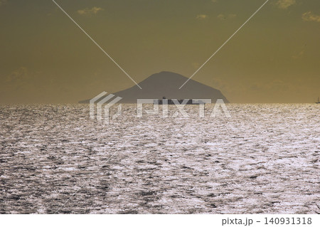 沖合に大島とコンテナ船がシルエットで浮かぶ夕刻近い海 140931318