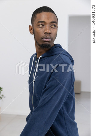 African American man wearing navy hoodie, standing and looking left in pale room with potted plant African American man wearing navy hoodie, standing and looking left in pale room with potted plant 140931372
