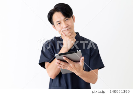 タブレットを見て悩む紺色のスクラブを着たミドル男性医師 タブレットを見て悩む紺色のスクラブを着たミドル男性医師 140931399