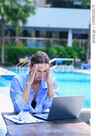 Overworked female freelancer having a headache while working remotely at a resort. Overworked female freelancer having a headache while working remotely at a resort. 140932075