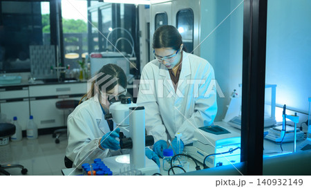 Two Female Scientists Working Together in Modern Research Laboratory with Microscope and Equipment Two Female Scientists Working Together in Modern Research Laboratory with Microscope and Equipment 140932149