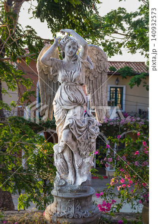 Classical white angel statue with wings in a garden courtyard with bougainvillea and Mediterranean-style building Classical white angel statue with wings in a garden courtyard with bougainvillea and Mediterranean-style building 140932573