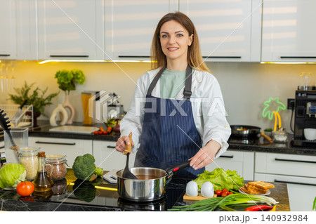 Middle-aged woman stirring hot soup in kitchen smiling healthy diet cooking for weight loss wellness Middle-aged woman stirring hot soup in kitchen smiling healthy diet cooking for weight loss wellness 140932984
