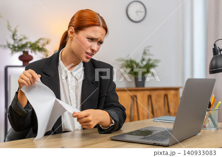 Young businesswoman tears draft report after error then opens new document typing eagerly on laptop Young businesswoman tears draft report after error then opens new document typing eagerly on laptop 140933083