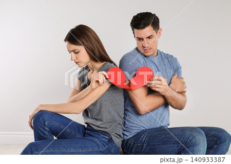 Couple with torn paper heart on light background. Relationship problems Couple with torn paper heart on light background. Relationship problems 140933387