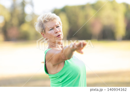 Senior woman exercising outdoors, stretching arm in park 140934162