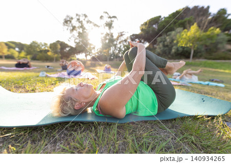 Senior woman practicing outdoor group yoga for wellness 140934265