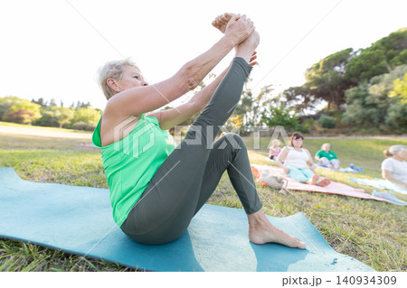Senior woman doing yoga stretching with group outdoors Senior woman doing yoga stretching with group outdoors 140934309