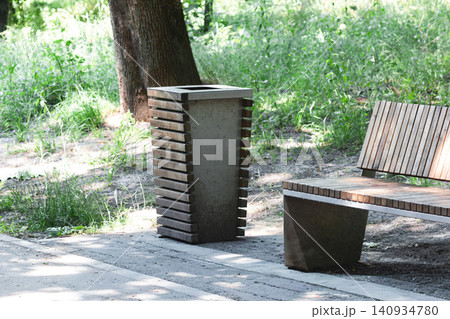 Modern wooden and concrete bench next to litter bin in sunny public park Modern wooden and concrete bench next to litter bin in sunny public park 140934780