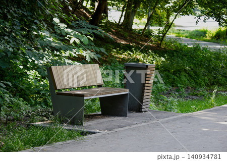 Modern wooden bench and trash can in a sunny summer park Modern wooden bench and trash can in a sunny summer park 140934781