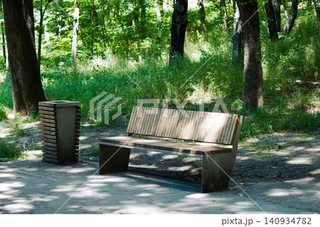 Modern wooden bench and trash can in a sunny summer park Modern wooden bench and trash can in a sunny summer park 140934782