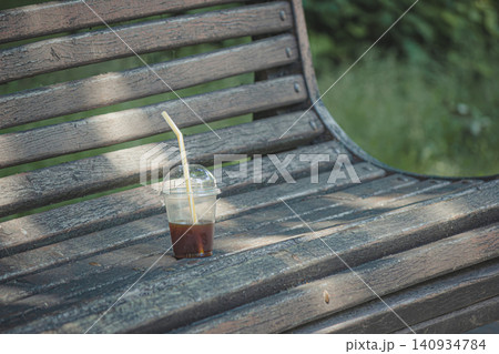 Plastic cup with leftover iced coffee on an old wooden park bench Plastic cup with leftover iced coffee on an old wooden park bench 140934784