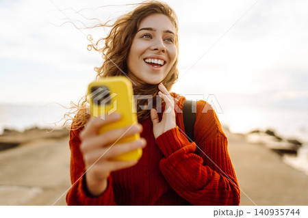 Young woman smiling and using her smartphone at the beach sunset. Blogging, communication concept. Young woman smiling and using her smartphone at the beach sunset. Blogging, communication concept. 140935744