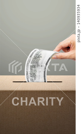 A hand putting a dollar bill into a cardboard charity box against a grey background. Concept of donation, philanthropy, and giving help to those in need A hand putting a dollar bill into a cardboard charity box against a grey background. Concept of donation, philanthropy, and giving help to those in need 140935934