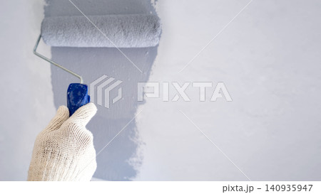 Close-up of a hand in a glove applying gray paint to a wall with a roller, leaving copy space 140935947