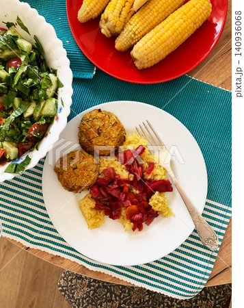 This meal features turmeric rice with vegetable fritters, baked vegetables, and boiled corn. A fresh salad accompanies the dish to create a balanced breakfast or lunch option 140936068
