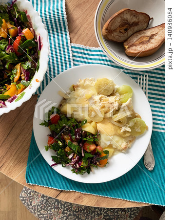 A meal features a plate with potatoes, fresh salad, a fried egg, and zucchini. Baked pears sit in a bowl nearby. The setting is a cozy wooden table with simple linens A meal features a plate with potatoes, fresh salad, a fried egg, and zucchini. Baked pears sit in a bowl nearby. The setting is a cozy wooden table with simple linens 140936084