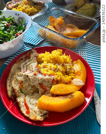 Dish includes turmeric rice, a vegetable omelette, and a fresh salad. Baked pumpkin adds a tasty option for breakfast or lunch on a table set with a striped cloth Dish includes turmeric rice, a vegetable omelette, and a fresh salad. Baked pumpkin adds a tasty option for breakfast or lunch on a table set with a striped cloth 140936122