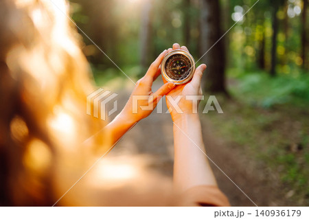 A hiker with curly hair holds a compass in their hands, carefully navigating through a sunlit forest A hiker with curly hair holds a compass in their hands, carefully navigating through a sunlit forest 140936179