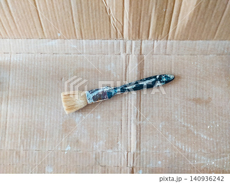 A worn paintbrush lies on a textured, dusty cardboard background, symbolizing creativity, home improvement, DIY projects, and artistic renovation. Ideal for craft and design concepts. 140936242