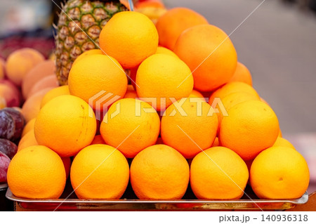 Fresh oranges stacked on a market stand near other fruits in a busy outdoor setting during daylight hours Fresh oranges stacked on a market stand near other fruits in a busy outdoor setting during daylight hours 140936318