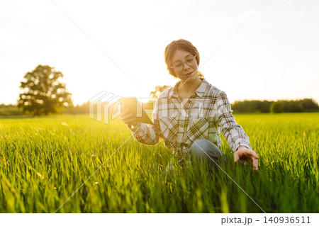 Young woman agronomist works on a modern digital tablet on a green wheat field. Young woman agronomist works on a modern digital tablet on a green wheat field. 140936511