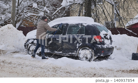 Person clearing snow from a car after a blizzard, facing winter weather challenges Person clearing snow from a car after a blizzard, facing winter weather challenges 140937854