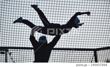 Athletic silhouette jumping high on a trampoline net, enjoying leisure and activity Athletic silhouette jumping high on a trampoline net, enjoying leisure and activity 140937894