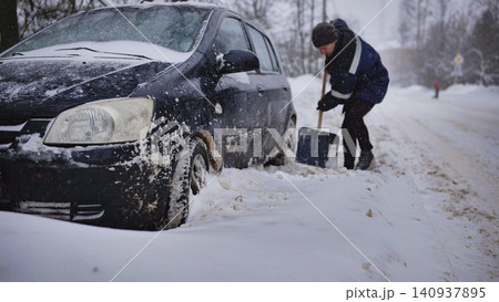 Man digging car out of deep snow during heavy blizzard, winter road conditions Man digging car out of deep snow during heavy blizzard, winter road conditions 140937895