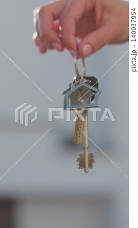 Vertical video A hand with a keychain in the shape of a small house and keys against the background of house. 140937954