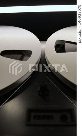 Vertical video Bobbin tape recorder. Old vintage reel-to-reel player. Vintage tape recorder roller. Reel film tape is rotating at a vintage professional player. 140938079