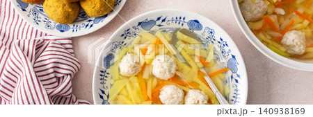 A bowl of vegetable soup with chicken meatballs is served alongside chickpea buns on a table. Fresh ingredients create a hearty meal for breakfast or lunch, banner A bowl of vegetable soup with chicken meatballs is served alongside chickpea buns on a table. Fresh ingredients create a hearty meal for breakfast or lunch, banner 140938169