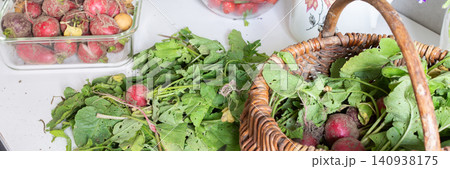 Baskets filled with fresh organic vegetables are placed on a wooden floor. Radishes, green onions, arugula, and lettuce create a colorful display of local produce, banner 140938175