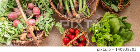 Baskets filled with fresh organic vegetables are placed on a wooden floor. Radishes, green onions, arugula, and lettuce create a colorful display of local produce, banner 140938203