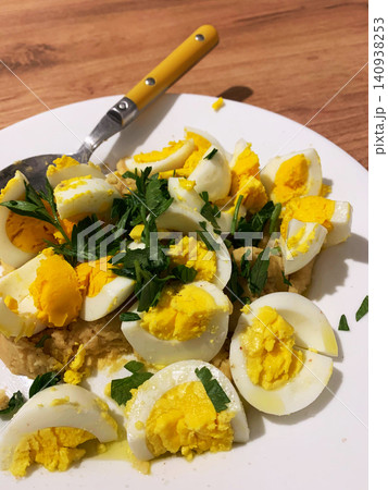 Millet porridge is topped with sliced boiled eggs and fresh herbs on a white plate. This dish is ready for a nutritious breakfast or lunch in a warm kitchen 140938253