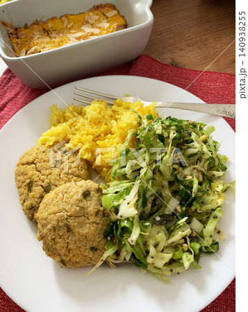 A cozy dining table features a plate of turmeric rice, zucchini meatballs, and a fresh salad. Beside it is a dish of gluten-free apple pie, ready to enjoy for lunch A cozy dining table features a plate of turmeric rice, zucchini meatballs, and a fresh salad. Beside it is a dish of gluten-free apple pie, ready to enjoy for lunch 140938255