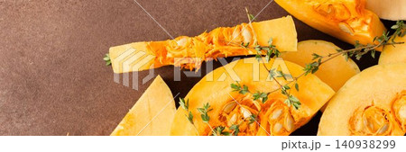 Yellow squash sliced into pieces is placed on a brown surface. Garlic cloves and fresh thyme are nearby, adding texture and color to the arrangement of vegetables, banner Yellow squash sliced into pieces is placed on a brown surface. Garlic cloves and fresh thyme are nearby, adding texture and color to the arrangement of vegetables, banner 140938299