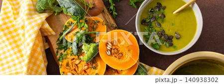 A table displays bowls of pumpkin soup with broccoli topped with seeds and herbs. Nearby, fresh ingredients and a pot hold more soup, creating a healthy meal setting, banner A table displays bowls of pumpkin soup with broccoli topped with seeds and herbs. Nearby, fresh ingredients and a pot hold more soup, creating a healthy meal setting, banner 140938302