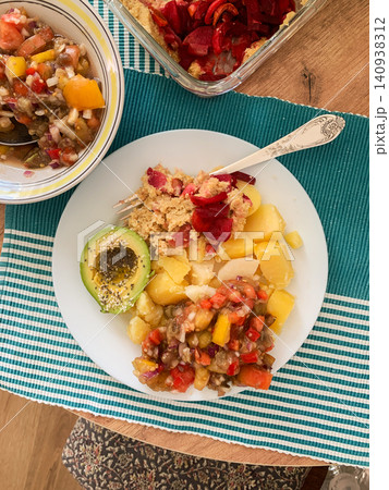 A plate holds a serving of potatoes with hummus and baked vegetables. Next to it is salad and avocado drizzled with olive oil and topped with sesame seeds A plate holds a serving of potatoes with hummus and baked vegetables. Next to it is salad and avocado drizzled with olive oil and topped with sesame seeds 140938312