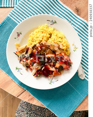A bowl of millet porridge is placed next to a generous serving of baked vegetables topped with pumpkin seeds. This nutritious dish is prepared and served at a cozy dining table 140938337
