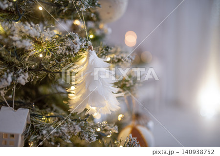 Decorative white feather ornament hanging from a beautifully adorned Christmas tree, surrounded by twinkling lights and festive decorations, creating a warm holiday atmosphere Decorative white feather ornament hanging from a beautifully adorned Christmas tree, surrounded by twinkling lights and festive decorations, creating a warm holiday atmosphere 140938752