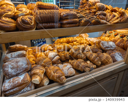Assorted fresh pastries and bread loaves arranged on shelves in a bakery display case, conveying a warm artisan atmosphere and appetizing variety for breakfast or dessert service Assorted fresh pastries and bread loaves arranged on shelves in a bakery display case, conveying a warm artisan atmosphere and appetizing variety for breakfast or dessert service 140939943
