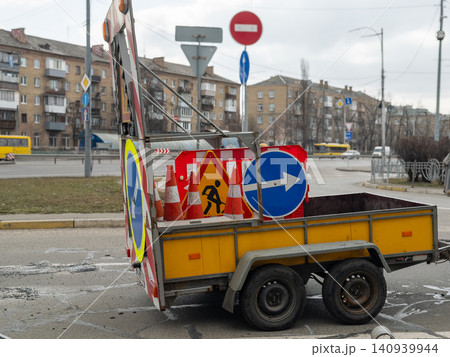 Road maintenance trailer loaded with orange cones and traffic warning signs parked on an urban street, conveying safety regulations and infrastructure repair projects in city traffic Road maintenance trailer loaded with orange cones and traffic warning signs parked on an urban street, conveying safety regulations and infrastructure repair projects in city traffic 140939944