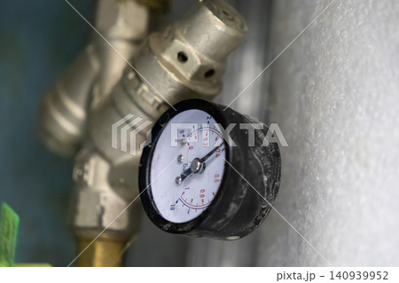 Industrial pressure gauge mounted on a metal plumbing valve indicates system load, representing technical maintenance, precision monitoring, and mechanical infrastructure control Industrial pressure gauge mounted on a metal plumbing valve indicates system load, representing technical maintenance, precision monitoring, and mechanical infrastructure control 140939952
