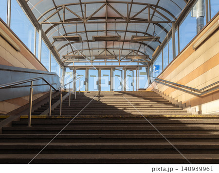Concrete staircase leading up to an enclosed pedestrian walkway with glass walls and metal roof structure, reflecting urban architecture and public transportation transit connection 140939961
