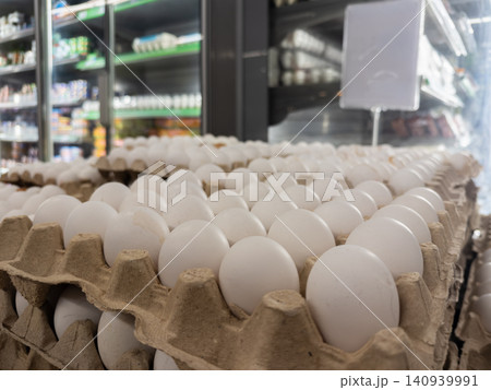 Fresh white chicken eggs are neatly arranged in cardboard cartons on a refrigerated supermarket shelf, showcasing an organized retail display of healthy protein food products today 140939991