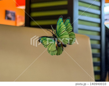 A green decorative butterfly model attached to a glass surface, creating an elegant nature-inspired accent for interior design and whimsical home wall decor in a modern living space 140940010
