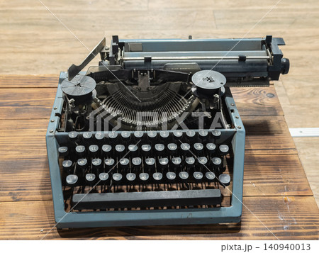 A vintage grey typewriter sits on a rustic wooden desk, serving as a classic creative writing tool that evokes nostalgic charm and traditional journalism in an old study room 140940013