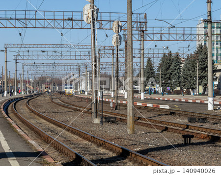 A passenger train approaches the platform along metal tracks at a railway station, depicting public transport infrastructure under a clear sky for urban commute and travel concepts A passenger train approaches the platform along metal tracks at a railway station, depicting public transport infrastructure under a clear sky for urban commute and travel concepts 140940026